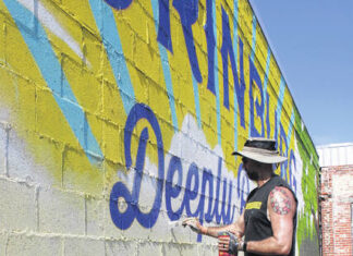 
			
				                                Muralist Max Dowdle is seen finishing up his second mural downtown in Laurinburg. The mural reads in large type “LAURINBURG” with the phrase “Deeply Rooted.”
                                 Tomeka Sinclair | The Laurinburg Exchange

			
		